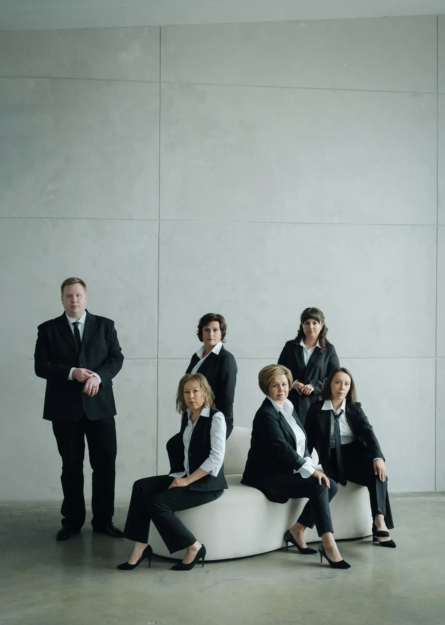An office team grouped around a low bench in black jackets and white collars