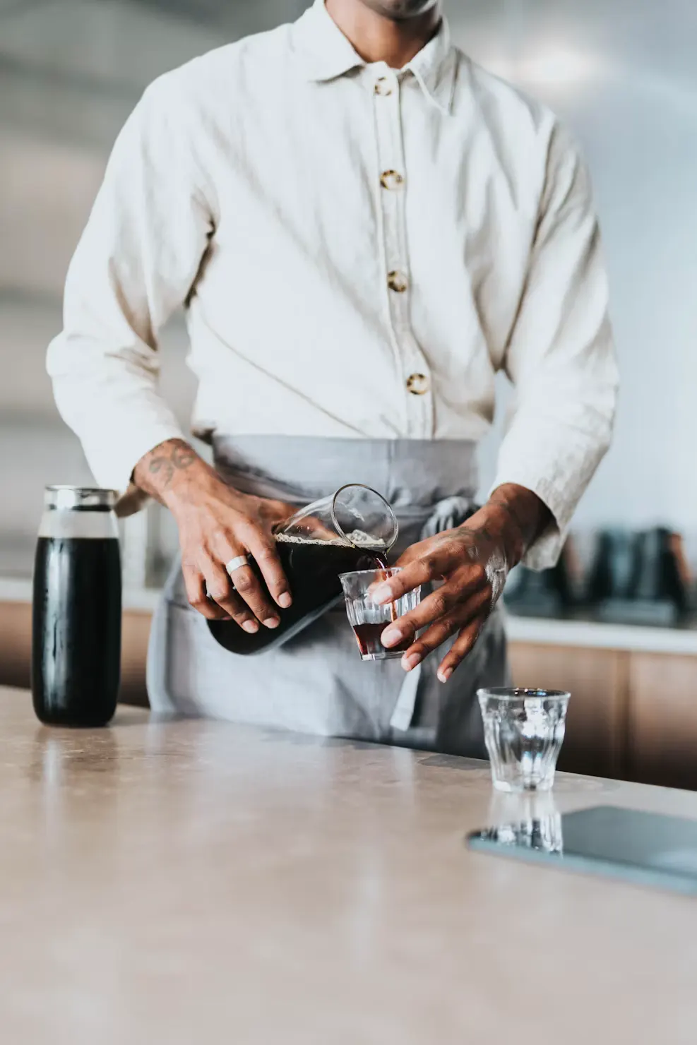 A member of service staff in apron and shirt making coffee behind a counter